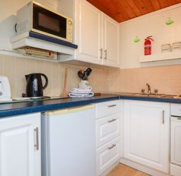 A kitchen corner with white cabinets a microwave kettle toaster sink stove and kitchen containers at Hawker's Cove near St Merryn