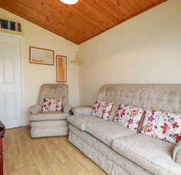 A living room with a sofa and armchair with floral cushions and wooden ceiling at Newtrain Bay near St Merryn
