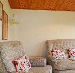 A living room with two floral armchairs a floral sofa with patterned cushions a wooden ceiling and wall shelf at Newtrain Bay near St Merryn