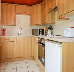 A kitchen with wooden cabinets a sink a microwave toaster and kettle at Newtrain Bay near St Merryn