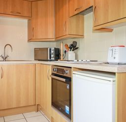 A kitchen with wooden cabinets a sink microwave oven toaster and kettle at Newtrain Bay near St Merryn