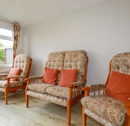 Three floral patterned armchairs with orange cushions in a room with wooden floor and white wall at Constantine Bay near St Merryn