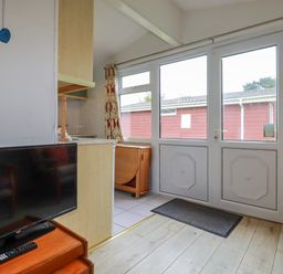 A room with a television on a wooden stand a door with windows and a chair near Constantine Bay near St Merryn
