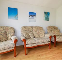 A living room with two armchairs and a two-seater sofa with floral upholstery and wooden legs at Porthcothan Bay in St Merryn