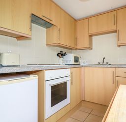A kitchen with wooden cabinets a white oven a small refrigerator a kettle a toaster and a microwave at Porthcothan Bay in St Merryn