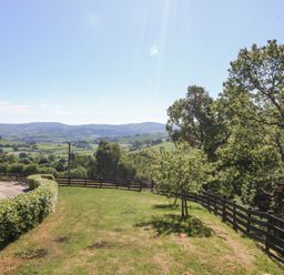 A grassy garden area with hedges and wooden fences overlooking rolling hills and trees at Holly Cottage in Llechwedd near Conwy