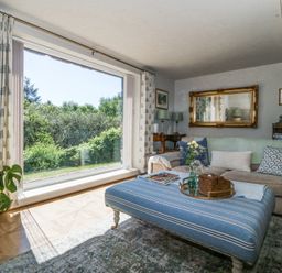 A living room with a large window overlooking greenery a striped ottoman and a sofa at Holly Cottage in Llechwedd near Conwy