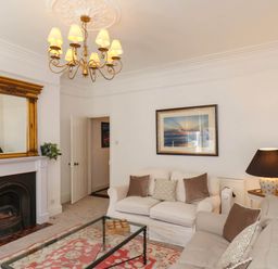 A living room with two sofas a glass coffee table a chandelier and a fireplace with a gold framed mirror at Flat 1 in Scarborough