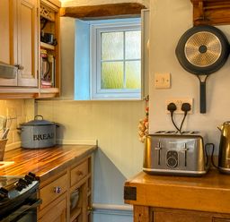 A kitchen counter with utensils in a pot a bread container a toaster a kettle and pans hanging on a wall at Lamorna Cottage in Chipping Norton