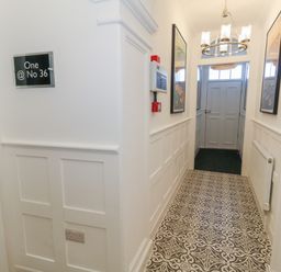 A hallway with patterned tile flooring white paneled walls a chandelier and framed artwork at Two @ No36 in Weymouth