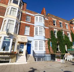 A row of brick and blue painted buildings including Bay View Hotel and a pop-up pizza place on a street in Weymouth