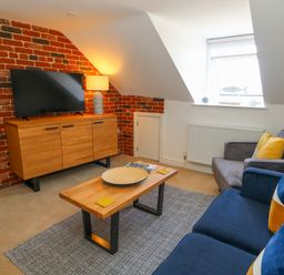 A living room with a blue sofa and wooden coffee table near a television on a wooden cabinet at The Loft @ No36 in Weymouth