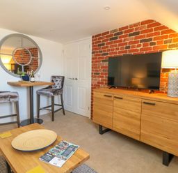 A small dining area with two bar stools and round mirror next to a wooden cabinet with a TV and lamp at The Loft @ No36 in Weymouth