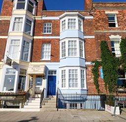 A street view of a multi-story brick building with blue and cream painted sections and signs for Bay View Hotel in Weymouth