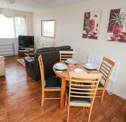 A living room with wooden dining table set and sofas facing a television at Freshwater East in Freshwater East