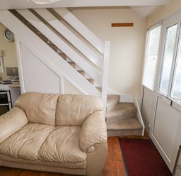 A small living area with a beige leather sofa next to a staircase and a door with windows and blinds at Freshwater East in Freshwater East