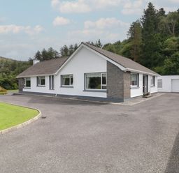 A single-story house with a driveway and garage surrounded by trees at Nelly's House in Gortahork County Donegal