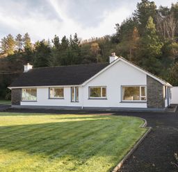 A single-story house with white walls and a dark roof next to a driveway and lawn at Nelly's House in Gortahork County Donegal