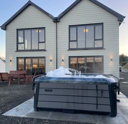 A hot tub with bubbles in front of a two-story house with outdoor wooden benches and tables at Little Pale Near Whitland