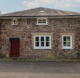Exterior of a two-story stone house with white framed windows and a red door at Clearbrook Lodge in Llanarthney nr Llandeilo Carmarthenshire