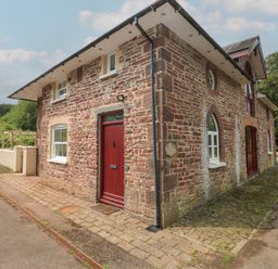A stone brick house with red doors and windows next to a paved path at Clearbrook Lodge in Llanarthney nr Llandeilo Carmarthenshire