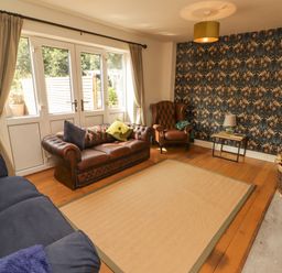 A living room with a brown leather sofa a blue sofa a brown armchair and a patterned wallpaper at Meadow Cottage in Llanarthney nr Llandeilo Carmarthenshire