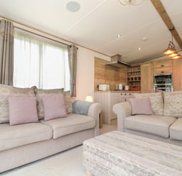 A living room with two sofas and an ottoman in front of a kitchen with wooden cabinets and appliances at Drake 11 in Cayton Bay