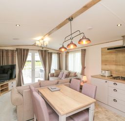 An open plan dining and living area with a dining table and chairs a sofa a TV and kitchen cabinets at Drake 11 in Cayton Bay