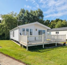 A white mobile home with a porch and railing on a grassy lot with trees in the background at 28 Finch in Cayton Bay