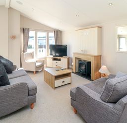 A living room with two grey sofas a beige armchair a wooden coffee table a fireplace and a television at 28 Finch in Cayton Bay