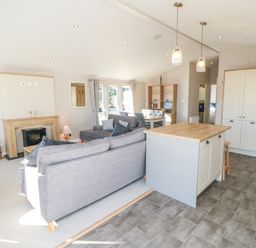An open plan living room and kitchen with grey sofas a wooden fireplace a kitchen island and dining table at 28 Finch in Cayton Bay