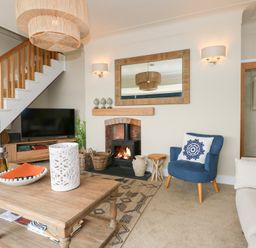 A living room with a wooden coffee table a blue armchair a fireplace and a television under stairs at Swn Y Wylan in Red Wharf Bay near Benllech