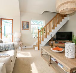 A living room with a sofa a wooden coffee table a television under stairs and a door leading to a conservatory at Swn Y Wylan Red Wharf Bay near Benllech