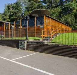 A wooden cabin with a fenced deck and umbrella surrounded by trees at Lakeland View Ambleside 86 White Cross Bay near Windermere