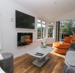 A living room with a wall-mounted tv and fireplace orange and gray seating and a coffee table at Lakeland View Ambleside 86 White Cross Bay near Windermere