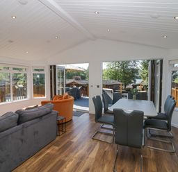 A dining area with a white table and six black chairs next to a living area with sofas and large windows at Lakeland View Ambleside 86 White Cross Bay near Windermere