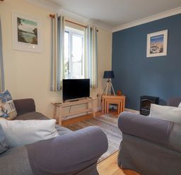 A living room with two grey sofas a wooden table with a television a window with striped curtains and blue and cream walls at Coombe Cottage in Falmouth