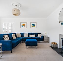 A living room with a blue sectional sofa a blue ottoman a wood burning stove and circular mirror at Fairwinds in Portreath