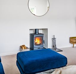 A living room with a wood burning stove fire and blue sofas at Fairwinds in Portreath