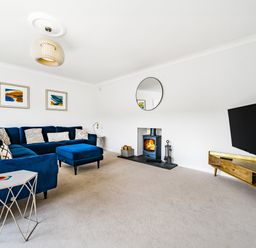 A living room with a blue sectional sofa a fireplace a wall-mounted TV and a wooden TV stand at Fairwinds in Portreath