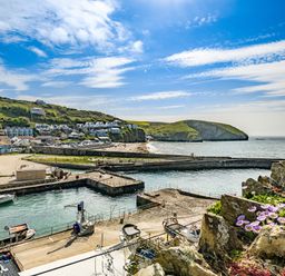 A harbor with boats docked near a beach and houses on a hill with cliffs and the sea in the background at Fairwinds in Portreath