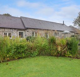 A stone building with multiple windows behind a garden with tall plants and grass at St Dogwells Barn near Wolfscastle
