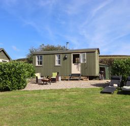 A small green corrugated cabin with outdoor seating and two lounge chairs on a grassy lawn at Shepherds Joy in Kennerleigh near Cheriton Fitzpaine