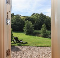 A garden with lounge chairs on grass viewed through an open door at Shepherds Joy Kennerleigh near Cheriton Fitzpaine
