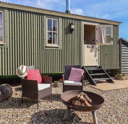 An outdoor seating area with two chairs and a fire pit in front of a green corrugated metal cabin at Shepherds Bliss in Kennerleigh near Cheriton Fitzpaine