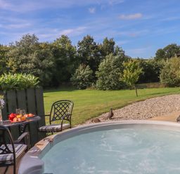 An outdoor seating area with a table and chairs next to a hot tub and a garden with trees at Shepherds Bliss in Kennerleigh near Cheriton Fitzpaine