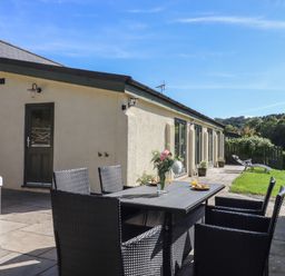 An outdoor patio with a dining table and chairs a hot tub and a lawn at Binneford Barn in Kennerleigh near Cheriton Fitzpaine