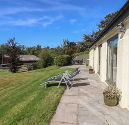 A patio with lounge chairs and potted plants beside a building with glass doors and a lawn at Binneford Barn Kennerleigh near Cheriton Fitzpaine
