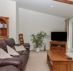 A living room with a brown leather sofa a wooden coffee table a TV on a wooden stand a bookshelf and a plant at Binneford Barn Kennerleigh near Cheriton Fitzpaine