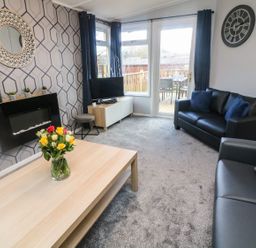 A living room with leather sofas a coffee table with flowers and a wall clock at Park View Lodge Arnside 7 South Lakeland Leisure Village near Carnforth